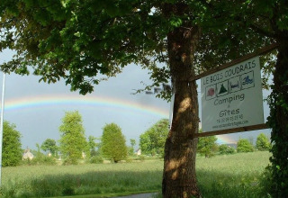 Arcobaleno sopra i campi verdi accanto al campeggio Le Bois Coudrais in Bretagna, Francia, con il cartello all’ingresso.