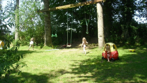 Bambini che giocano su un prato con altalene e una macchinina sotto gli alberi al campeggio Le Bois Coudrais in Bretagna.