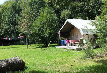 Safari tent at Campsite Le Bois Coudrais in France, nestled in lush greenery with trees and open grass.