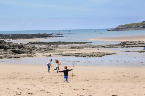 Bambini che giocano su una spiaggia vicino a Cuguen, Bretagna, Francia, con rocce e mare sullo sfondo.