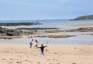Bambini che giocano su una spiaggia vicino a Cuguen, Bretagna, Francia, con rocce e mare sullo sfondo.