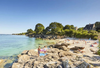 Spiaggia soleggiata con rocce, persone e una casa tra il verde vicino a Cuguen, Bretagna, Francia.