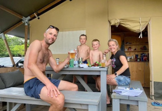 Una familia sonríe y comparte comida y bebidas afuera de su tienda de safari en un campamento.