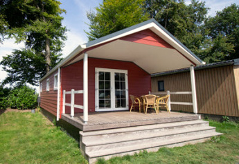 Rood Luxe chalet met overdekte veranda, tuinmeubilair en houten traptreden te midden van groen.