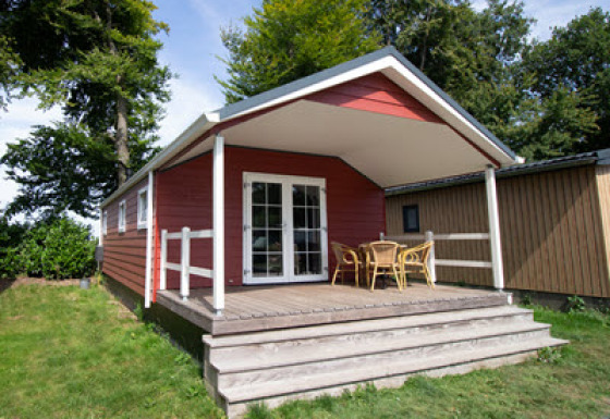 Red Luxe chalet with a covered porch, outdoor furniture, and wooden steps surrounded by greenery.