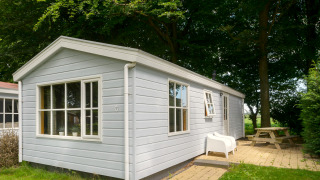 Buitenaanzicht van de Chalet-lodge met lichtblauwe houten gevel, witte ramen en terras met zitje.