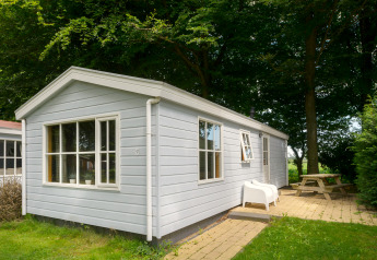 Buitenaanzicht van de Chalet-lodge met lichtblauwe houten gevel, witte ramen en terras met zitje.