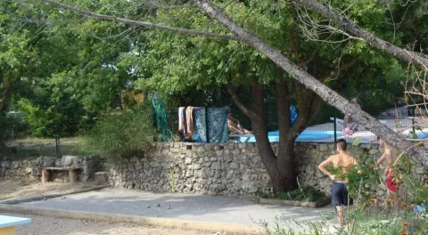 Due ragazzi giocano a pétanque vicino a un muro di pietra con piscina e asciugamani in campeggio in Provenza.