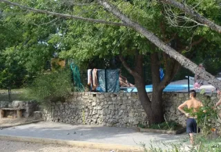 To drenge spiller petanque ved en stenmur med pool og håndklæder i en skovklædt campingplads i Provence.