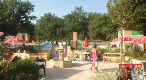 Buitenruimte van Camping Avelanède met zwembad, rode parasols, tafels en mensen in Provence-Alpes-Côte d’Azur.