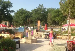 Buitenruimte van Camping Avelanède met zwembad, rode parasols, tafels en mensen in Provence-Alpes-Côte d’Azur.