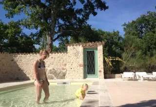 A woman and small child play in a shallow pool by a stone wall at Campsite Avelanède, Provence, France.