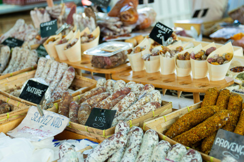 Assorted traditional French sausages and cured meats arranged on a market stall with flavor signs visible.