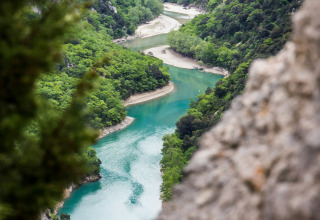 Blick auf einen sich windenden türkisfarbenen Fluss durch grüne Hügel bei Campsite Avelanède in Provence-Alpes-Côte d’Azur, Frankreich.
