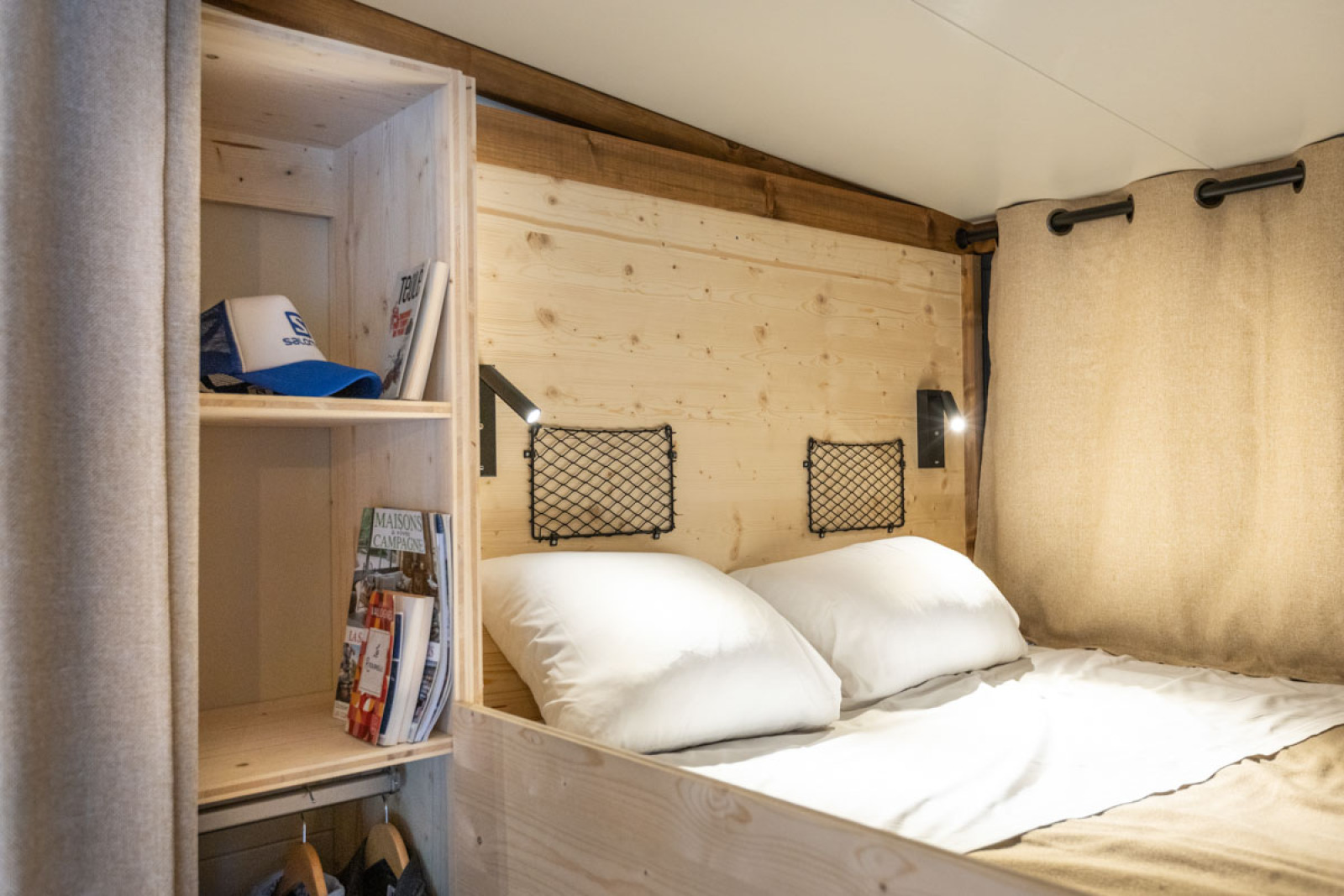 Slaapruimte met houten panelen, bed en plankjes in de Arizona safaritent bij Huttopia Lac de Serre Ponçon, Frankrijk.