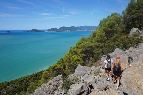 Wandelaars op een kustpad nabij Montescudaio, Toscane, met zicht op zee en bosrijke heuvels.