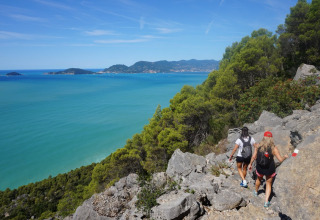 Wandelaars op een kustpad nabij Montescudaio, Toscane, met zicht op zee en bosrijke heuvels.