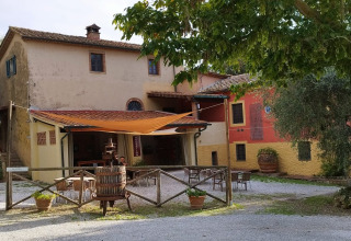 Boerderijwoning met buitenzitje en bomen bij Agricampeggio La Prugnola, een vakantiepark in Toscane, Italië.