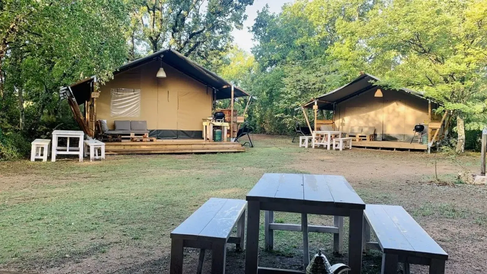 Twee safaritenten op camping Avelanède in Frankrijk, met picknicktafels en banken tussen de bomen.