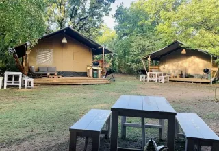 Due tende safari al campeggio Avelanède in Francia, con tavoli da picnic e panche tra gli alberi.
