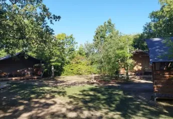 Tiendas tipo safari en el camping Avelanède en Francia, rodeadas de árboles y sombra bajo el cielo azul.
