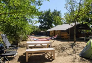 Campeggio all'aperto con tenda safari, amaca, tavolo da picnic e sedie al Campeggio Avelanède in Francia.