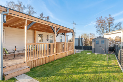 Ampia veranda in legno e prato verde presso Vakantiehuis Admiral, con sedute e casetta da giardino.