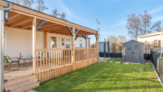 Ampia veranda in legno e prato verde presso Vakantiehuis Admiral, con sedute e casetta da giardino.