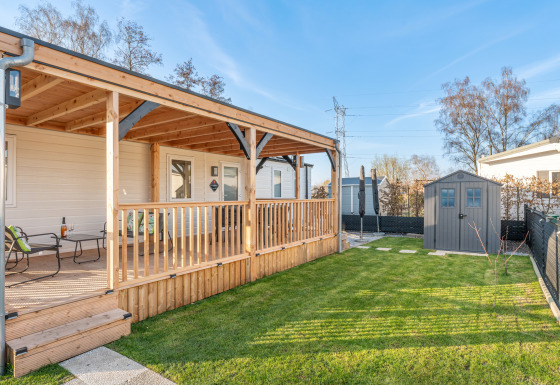 Ampia veranda in legno e prato verde presso Vakantiehuis Admiral, con sedute e casetta da giardino.