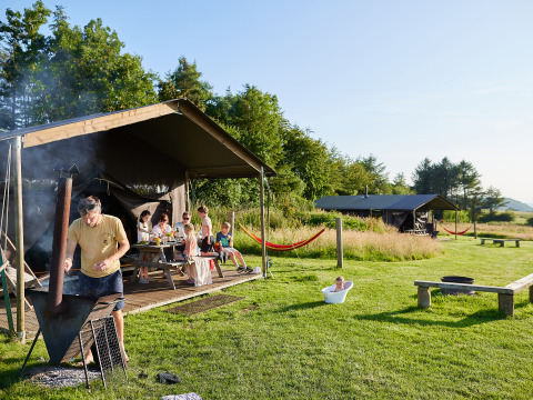 Familie genießt Grillen und Entspannung vor Zelten im BoerenBed Warren Farm Ferienpark in Südwestengland.