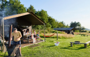 Familie griller og hygger foran telt ved BoerenBed Warren Farm feriepark i det sydvestlige England om sommeren.