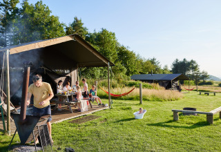 Familie genießt Grillen und Entspannung vor Zelten im BoerenBed Warren Farm Ferienpark in Südwestengland.
