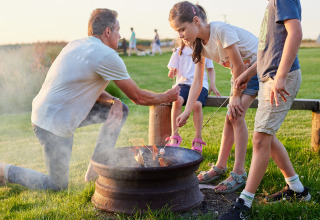 Family toasting marshmallows over a fire pit at BoerenBed Warren Farm holiday park in South West England.