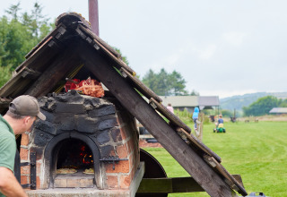 Hombre cocinando en un horno de leña al aire libre en BoerenBed Warren Farm, parque vacacional del suroeste de Inglaterra.