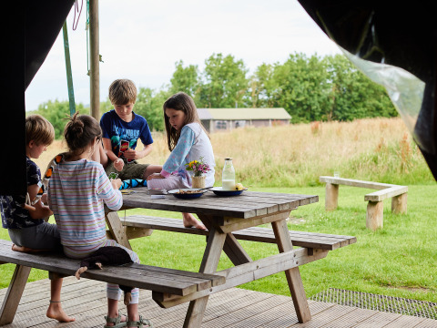 Children play together at a wooden picnic table at BoerenBed Warren Farm holiday park in South West England.