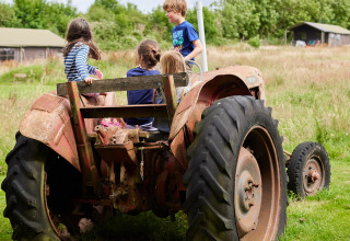 Niños jugando y sentados en un tractor antiguo en BoerenBed Warren Farm, parque vacacional en el sudoeste de Inglaterra.