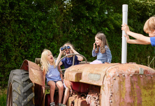 Kinder spielen fröhlich auf einem alten Traktor bei BoerenBed Warren Farm in Südwestengland.