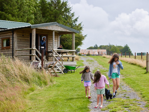 Drie kinderen wandelen met een hond bij een houten hut op BoerenBed Warren Farm in Zuidwest-Engeland.