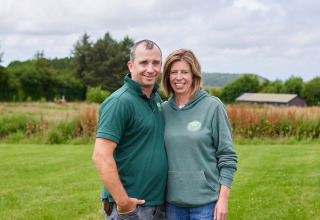 Ein lächelndes Paar steht auf einer Wiese bei BoerenBed Warren Farm, einem Ferienpark in Südwestengland.