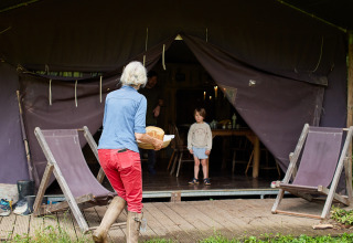 Woman in red pants and boots brings bread to a child outside a tent at BoerenBed Upper Shadymoor Farm, Wales.