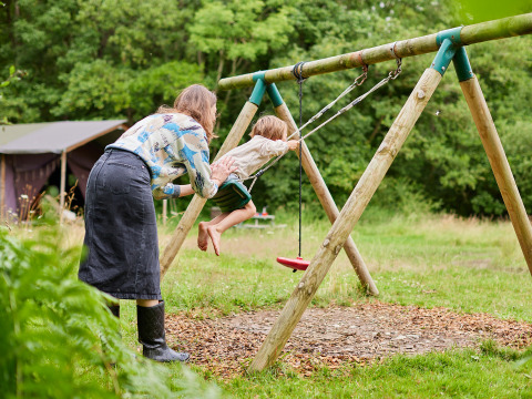 Un adulto spinge un bambino sull'altalena nell'area giochi di BoerenBed Upper Shadymoor Farm in Galles, Regno Unito.