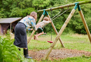 An adult pushes a child on a swing at the outdoor play area of BoerenBed Upper Shadymoor Farm in Wales, UK.
