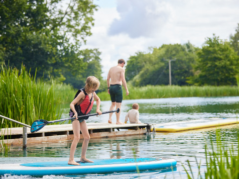 Kinderen en volwassenen genieten van suppen en ontspannen aan een meer op Upper Shadymoor Farm in Wales.
