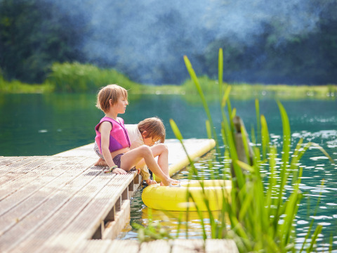 Due bambini con giubbotti di salvataggio siedono su un molo di legno a BoerenBed Upper Shadymoor Farm, Galles.