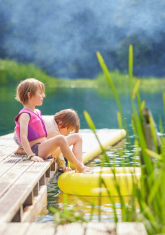 Due bambini con giubbotti di salvataggio siedono su un molo di legno a BoerenBed Upper Shadymoor Farm, Galles.