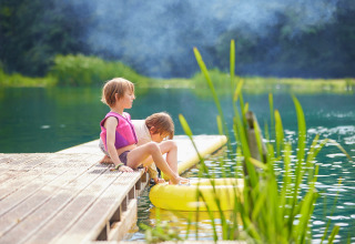 Dos niños con chalecos salvavidas se sientan en un muelle de madera en BoerenBed Upper Shadymoor Farm, Gales.