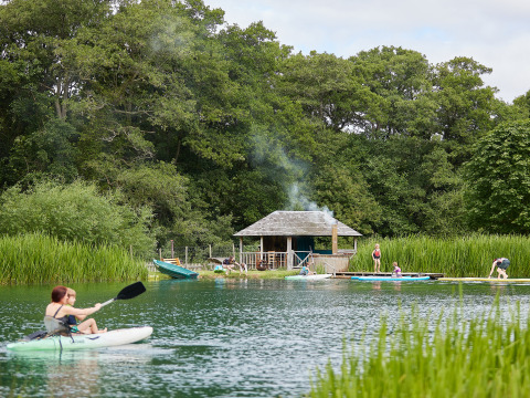 Persone fanno kayak e paddle board su un lago vicino a una casetta a BoerenBed Upper Shadymoor Farm, Galles.