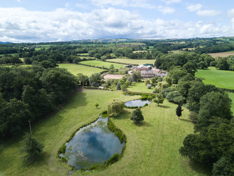 Veduta aerea di BoerenBed Upper Shadymoor Farm in Galles, UK, con stagni, campi e paesaggio verde.
