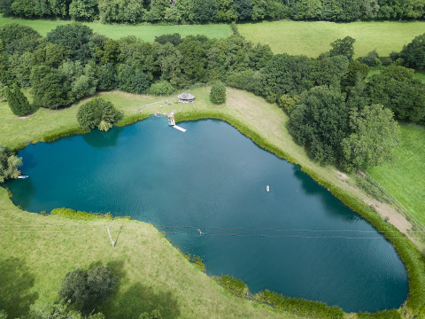 Vista aérea de un lago rodeado de campos verdes y bosque en BoerenBed Upper Shadymoor Farm, Gales, Reino Unido.