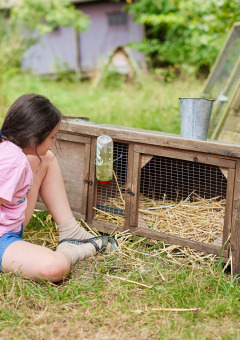 Een meisje zit in het gras bij een houten konijnenhok op BoerenBed New Barn Farm in Oost-Engeland.